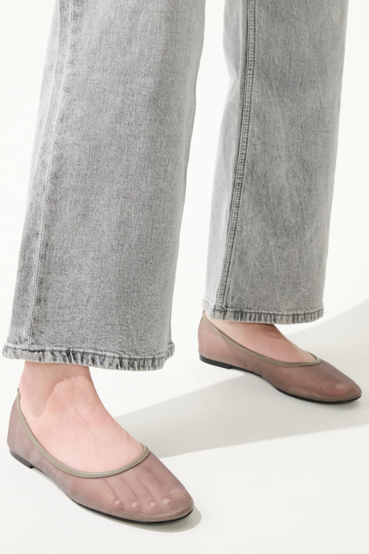 Person wearing gray jeans and pink flats on a white background
