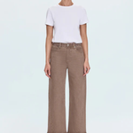 A model stands against a light gray studio background wearing a white short-sleeve crewneck t-shirt tucked into high-waisted, wide-leg brown cropped jeans, paired with beige strappy high-heeled sandals.