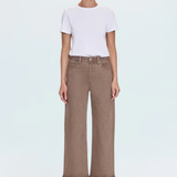 A model stands against a light gray studio background wearing a white short-sleeve crewneck t-shirt tucked into high-waisted, wide-leg brown cropped jeans, paired with beige strappy high-heeled sandals.