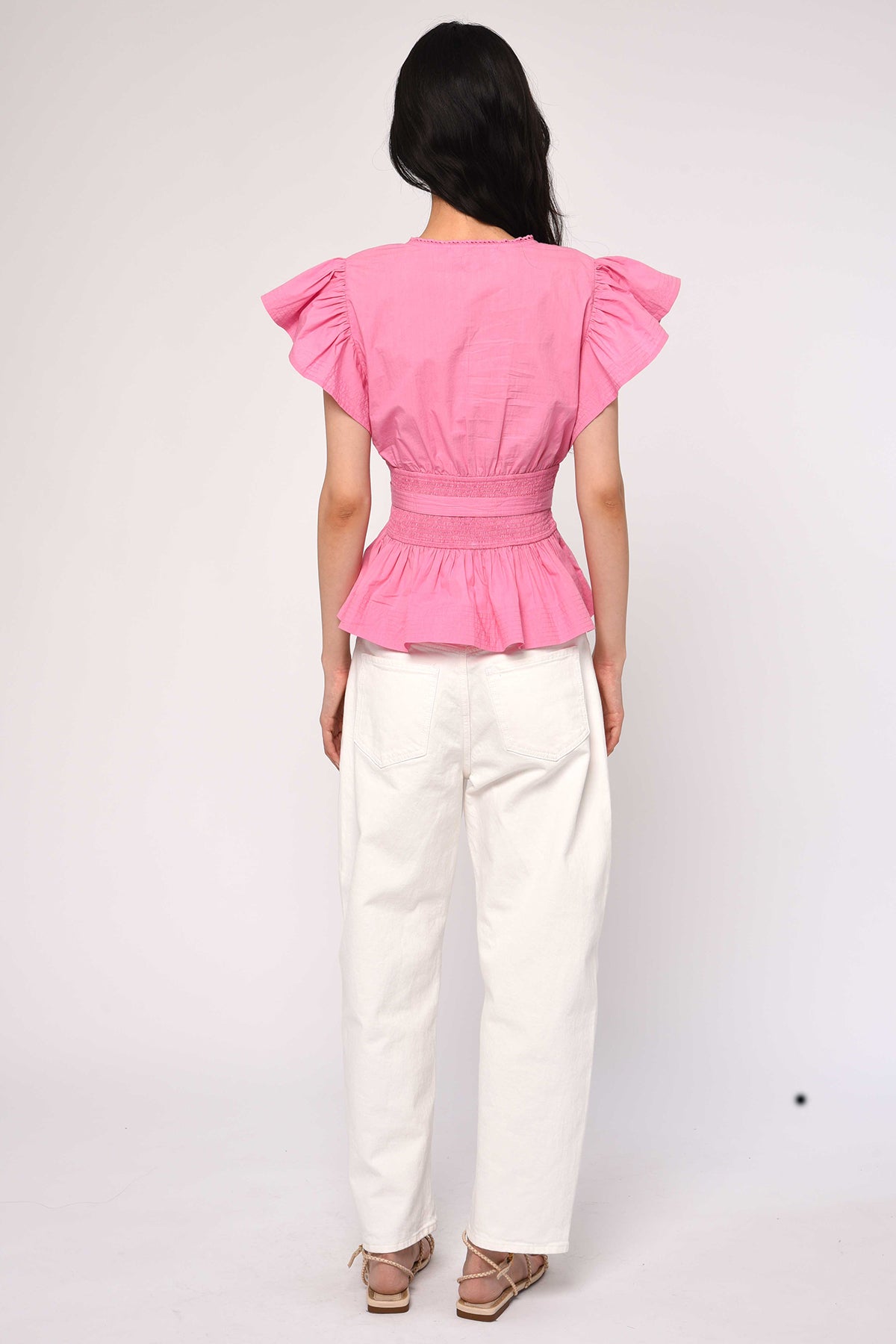 Person wearing a pink top with ruffled sleeves and white pants on a white background