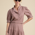 A woman modeling a brown and white gingham tiered dress with puff sleeves and a high collar, styled with black sunglasses against a solid beige background.