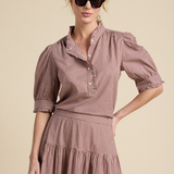 A woman modeling a brown and white gingham tiered dress with puff sleeves and a high collar, styled with black sunglasses against a solid beige background.