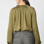 A woman shown from the back wearing a long-sleeve olive green blouse with a gathered, pleated high neckline and grey textured trousers, against a plain light gray background.