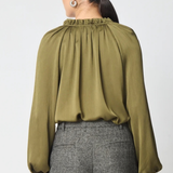 A woman shown from the back wearing a long-sleeve olive green blouse with a gathered, pleated high neckline and grey textured trousers, against a plain light gray background.