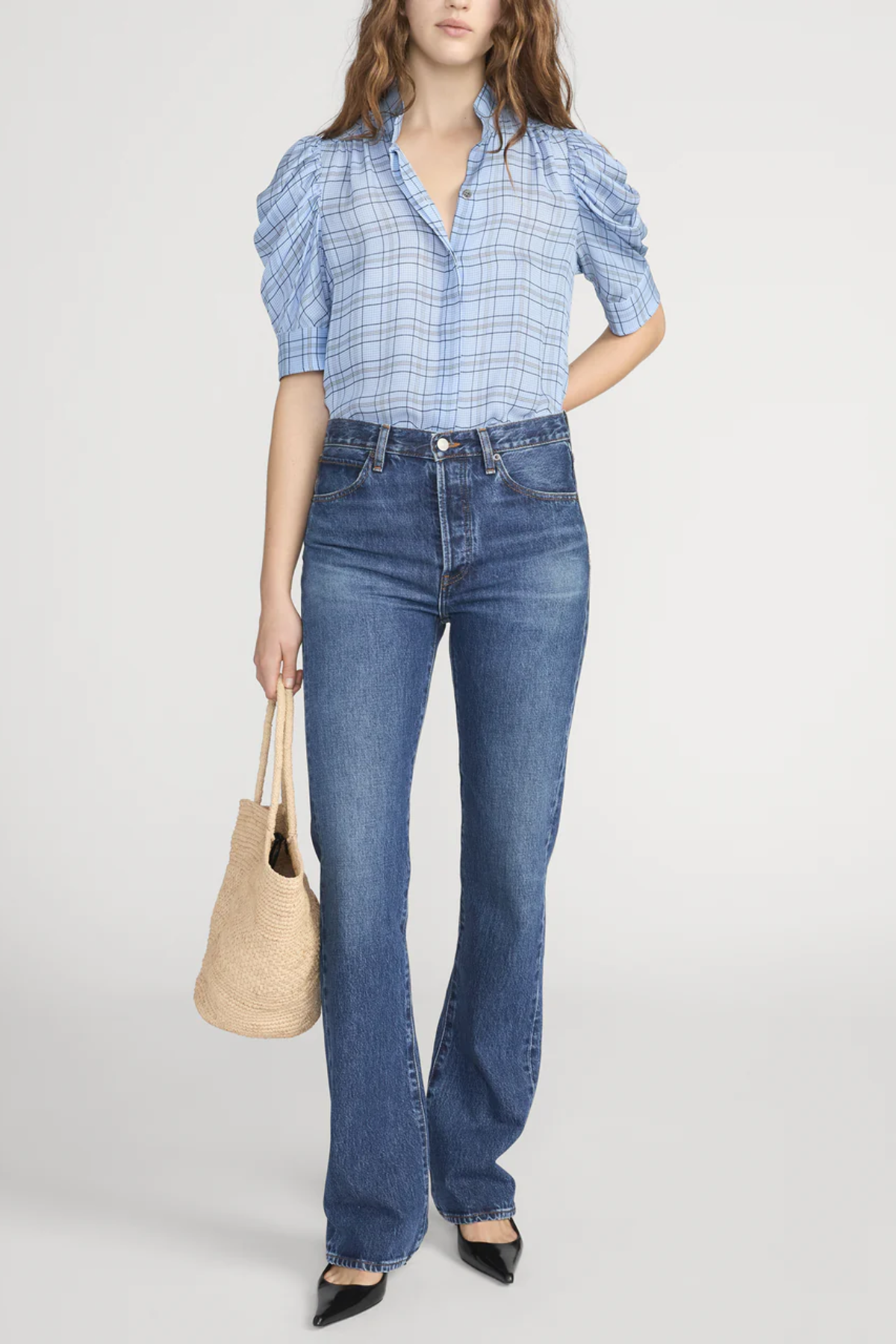 Woman wearing a blue checkered blouse and jeans holding a beige bag on a white background