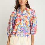 Woman wearing a colorful floral shirt and beige shorts on a plain background