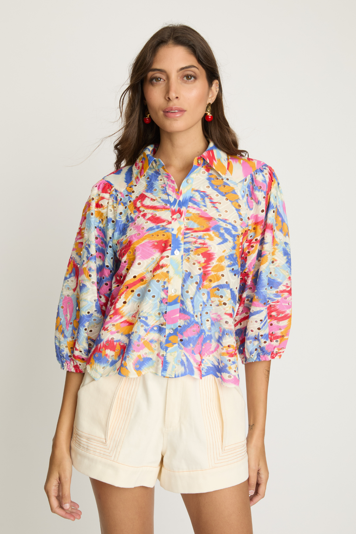 Woman wearing a colorful floral shirt and beige shorts on a plain background