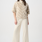 Woman wearing a beige poncho over a white outfit on a white background