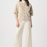 Woman wearing a beige poncho over a white outfit on a white background