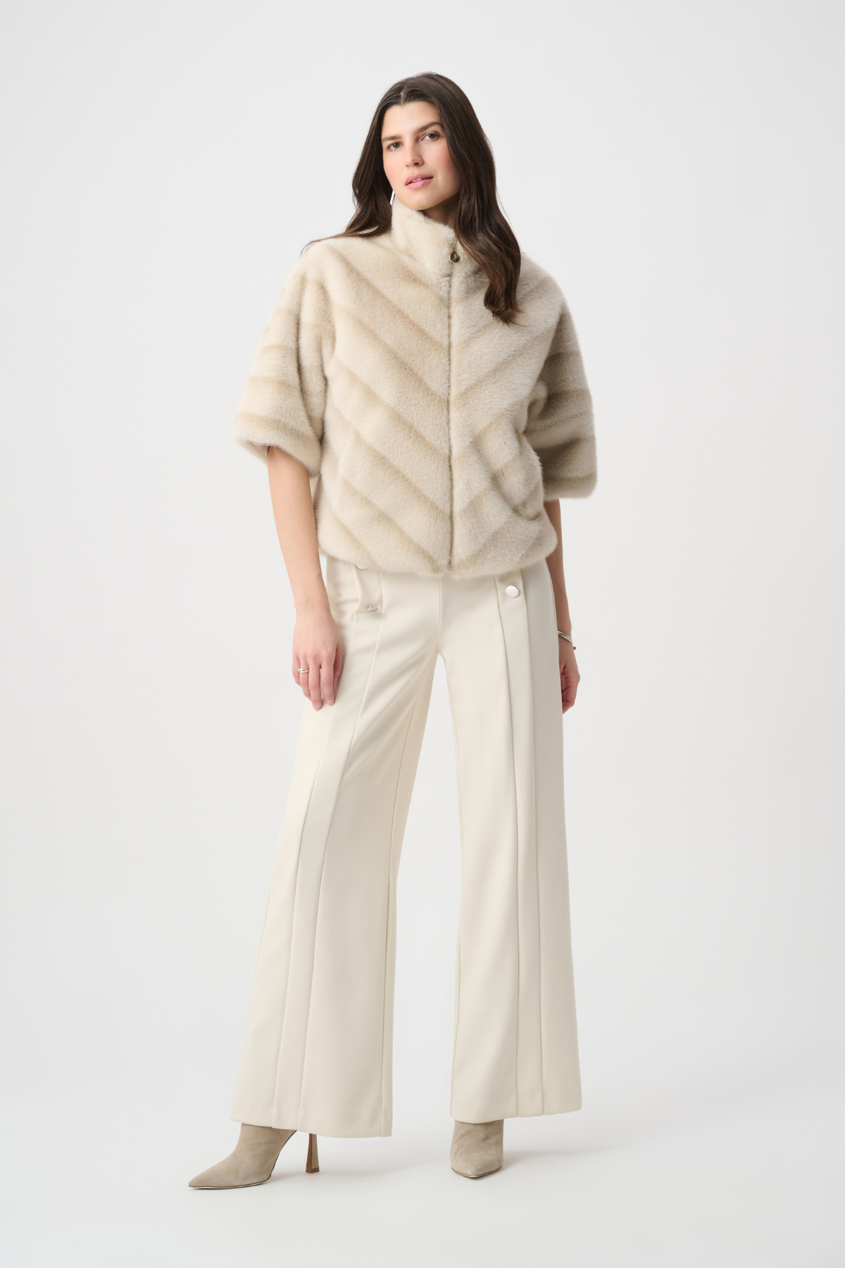 Woman wearing a beige poncho over a white outfit on a white background