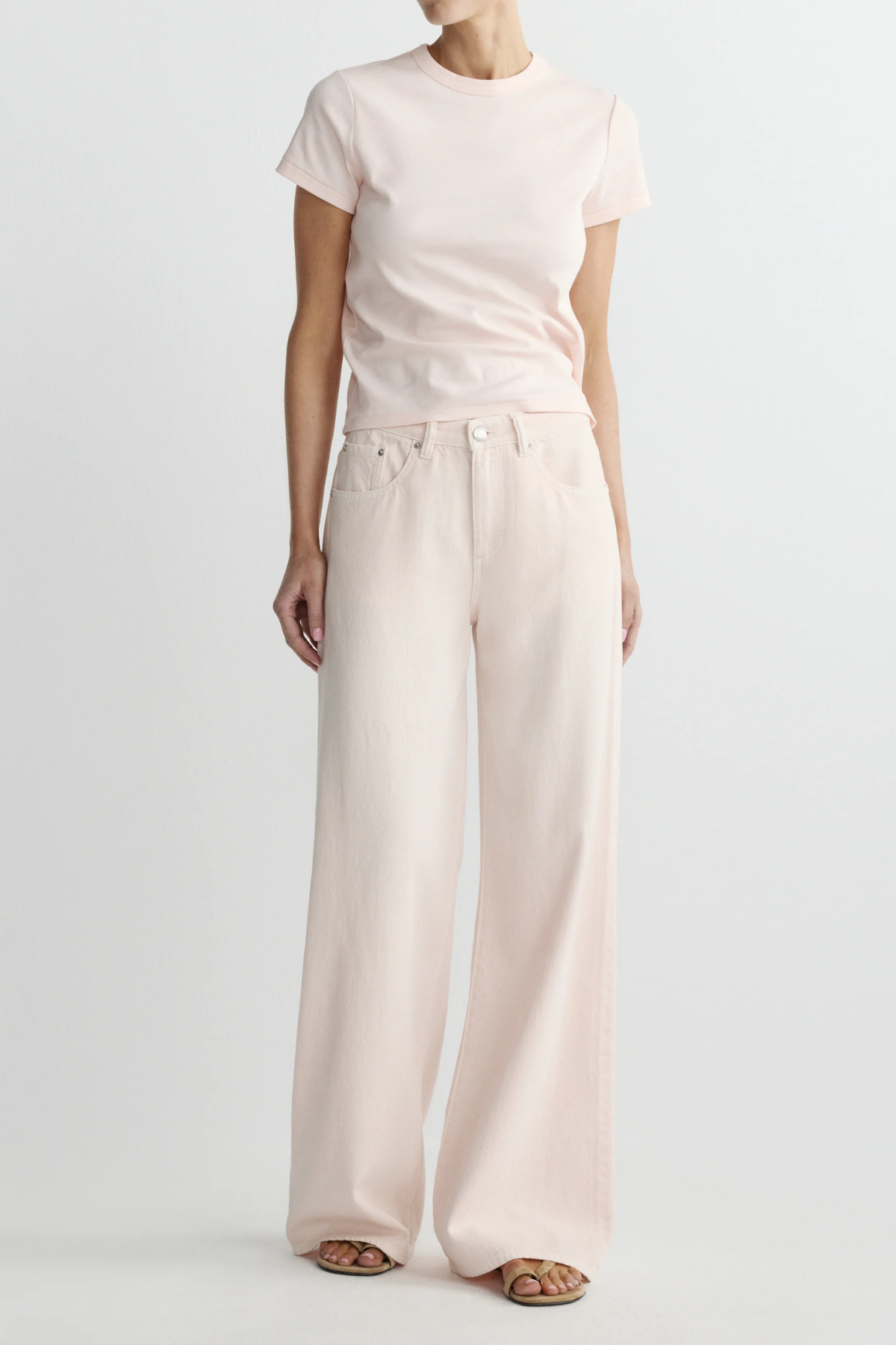 Person wearing a white t-shirt and light pink wide-leg pants on a plain background