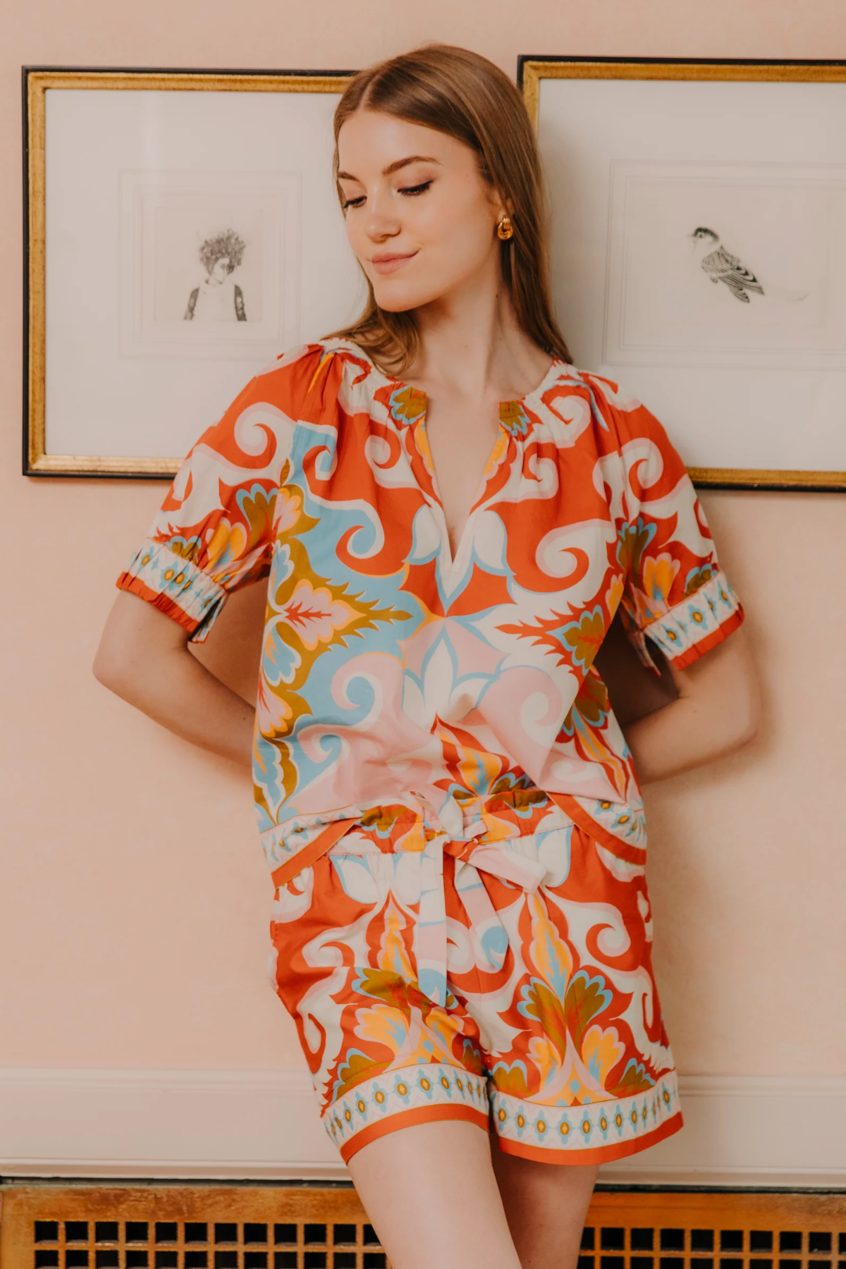 Woman wearing a colorful patterned dress standing against a light pink wall.