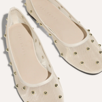 A pair of cream-colored ballet flats with a textured fabric upper and gold-tone metal studs, shown from a top-down angle on a light beige background.