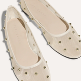 A pair of cream-colored ballet flats with a textured fabric upper and gold-tone metal studs, shown from a top-down angle on a light beige background.