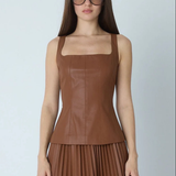 A woman modeling a brown faux-leather sleeveless top with a square neckline and matching pleated skirt against a light gray background.