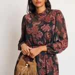 Woman wearing a floral dress holding a brown fringed bag against a white background