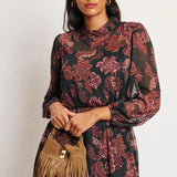Woman wearing a floral dress holding a brown fringed bag against a white background