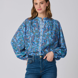 Woman wearing a blue patterned blouse and jeans on a gray background