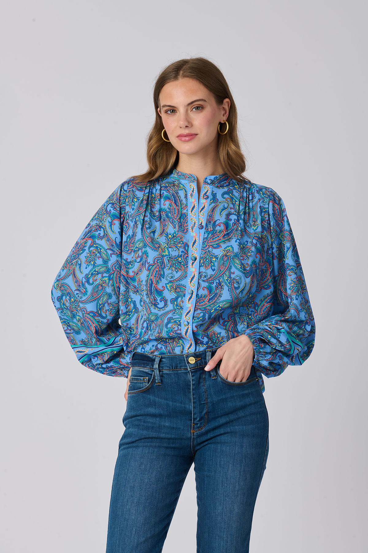 Woman wearing a blue patterned blouse and jeans on a gray background