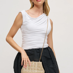 Woman wearing a white sleeveless top and black skirt holding a beige handbag on a plain background