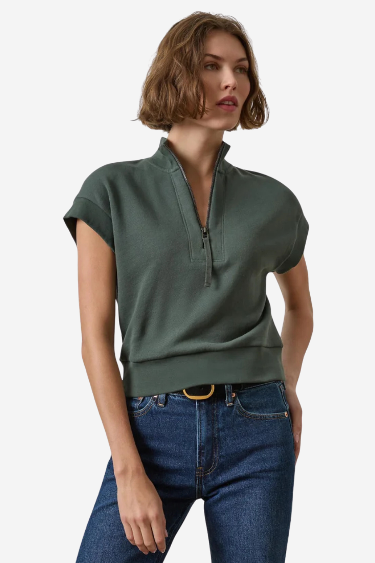 A woman modeling a dark green short-sleeve quarter-zip knit top with a ribbed hem, paired with blue jeans, against a plain light gray background.