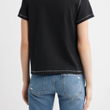 A woman shown from the back wearing a black short-sleeve t-shirt with white contrast stitching and blue jeans, against a plain white studio background.