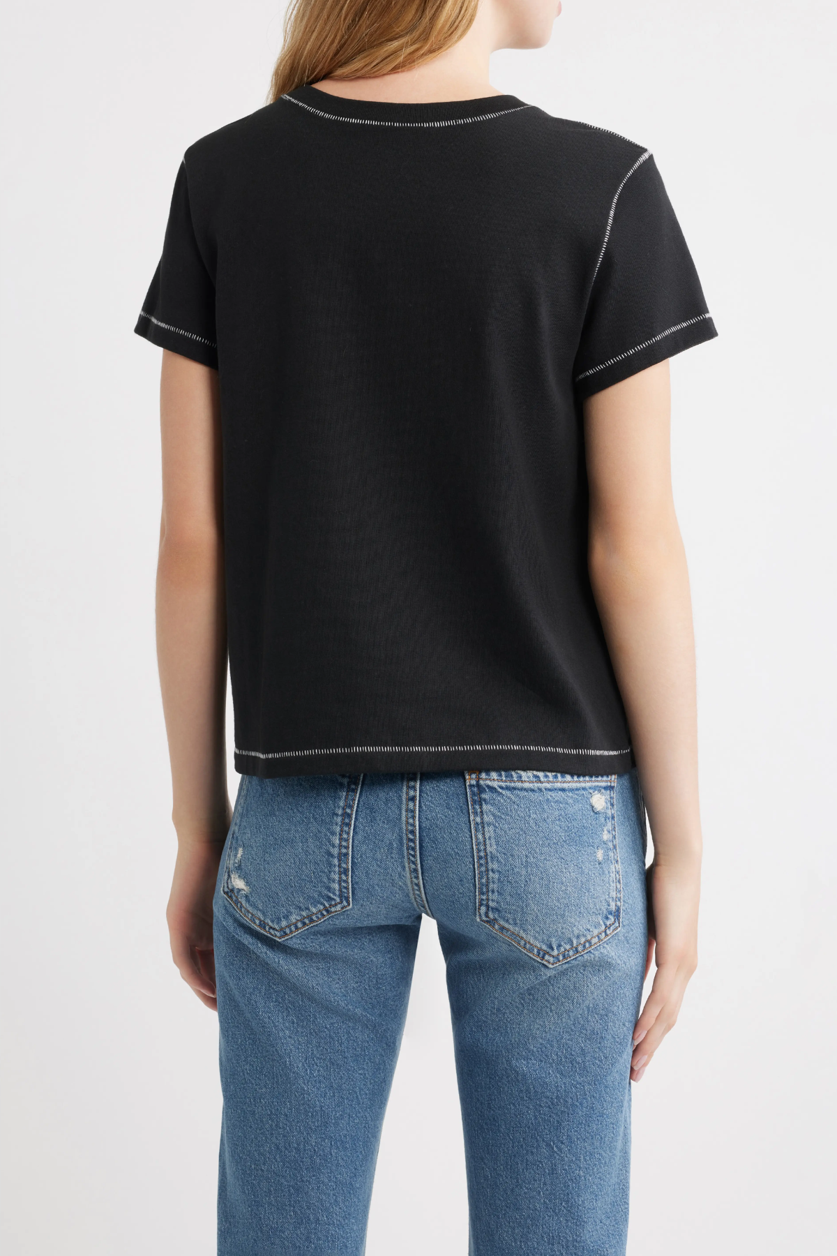 A woman shown from the back wearing a black short-sleeve t-shirt with white contrast stitching and blue jeans, against a plain white studio background.