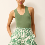 Woman wearing a green sleeveless top and leaf-patterned shorts on a plain background