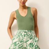 Woman wearing a green sleeveless top and leaf-patterned shorts on a plain background