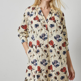 A woman modeling a cream-colored long-sleeve shirt dress with a red and navy blue floral print, set against a plain light gray studio background.