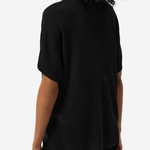 A woman shown from the back wearing a black short-sleeve knit top and black pants against a plain light gray studio background.