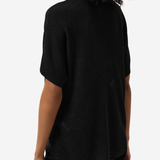 A woman shown from the back wearing a black short-sleeve knit top and black pants against a plain light gray studio background.