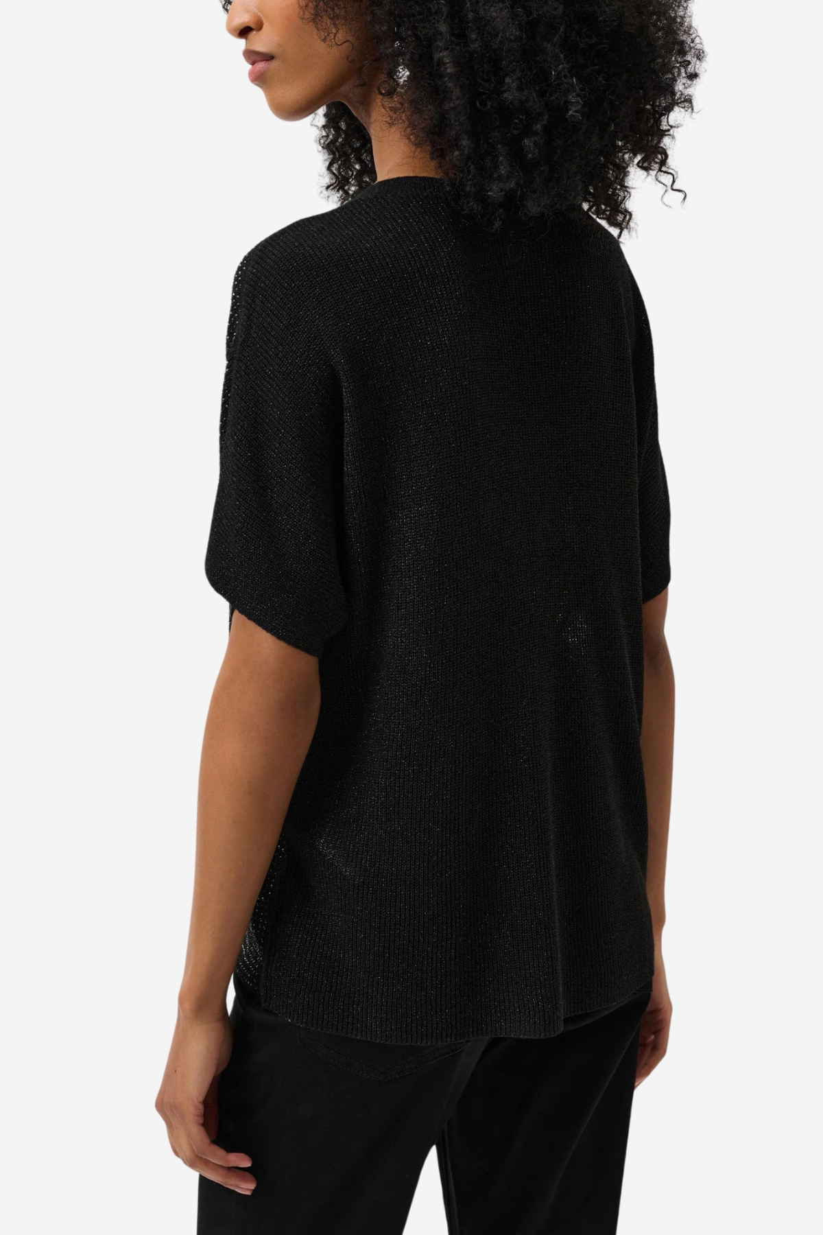 A woman shown from the back wearing a black short-sleeve knit top and black pants against a plain light gray studio background.