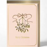 A vertical Christmas greeting card with a pale blush pink background, featuring an illustration of mistletoe with a gold border and the words 'Merry Christmas' in gold at the bottom. The card is shown standing upright with a metallic gold envelope behind it on a light gray background.