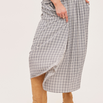 A person wearing a high-waisted, wide-leg plaid skirt in a black and white check pattern, styled with tan suede boots against a plain off-white studio background.