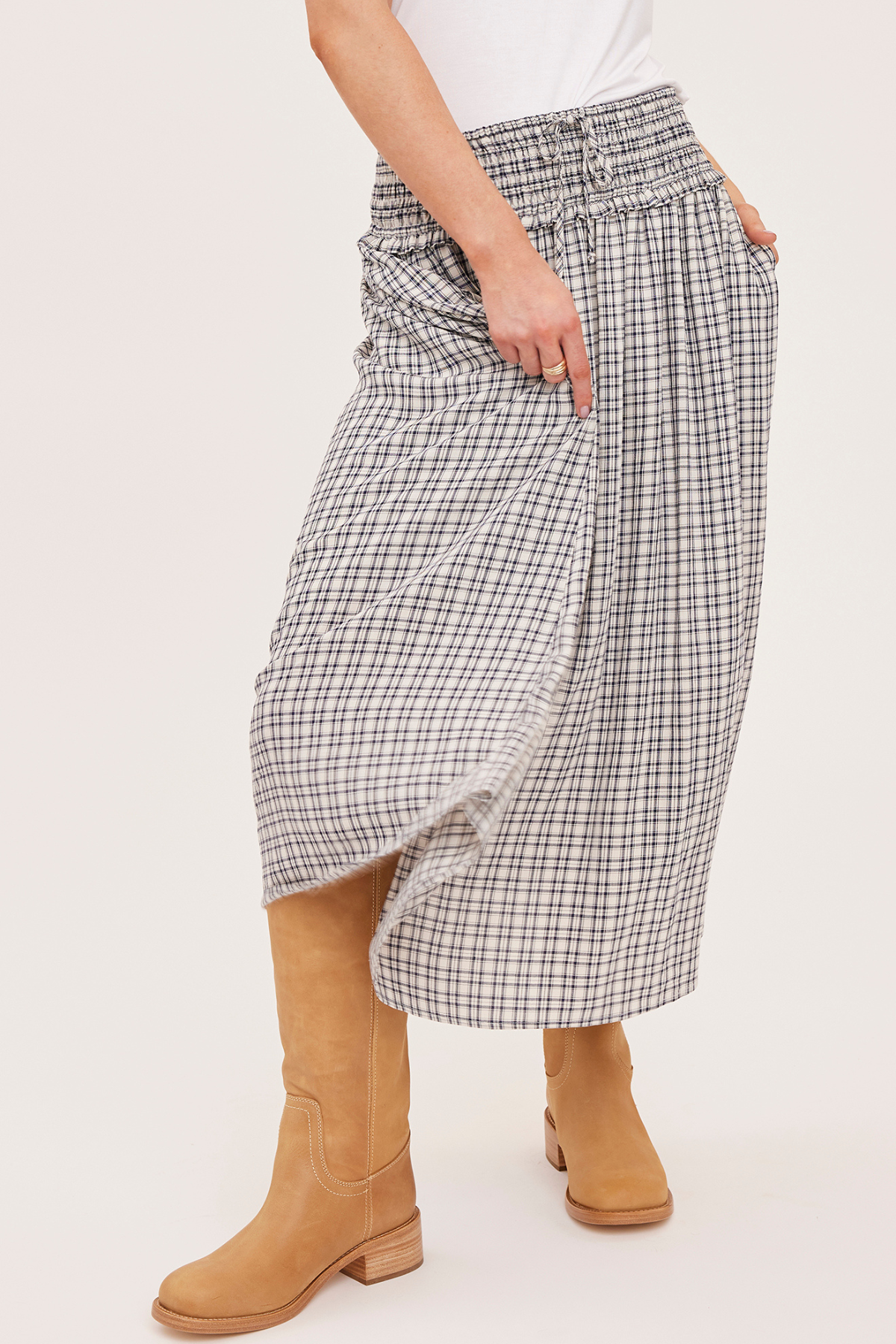 A person wearing a high-waisted, wide-leg plaid skirt in a black and white check pattern, styled with tan suede boots against a plain off-white studio background.