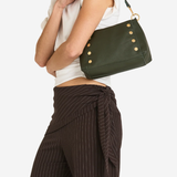A model wearing a white sleeveless top and dark brown pinstriped wrap pants carries an olive green leather shoulder bag with gold-tone studs and a black strap against a light gray background.