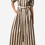 A woman wearing a brown and cream vertical striped midi shirt dress with puff sleeves, a button-up front, and a matching belt, paired with brown heeled sandals against a light gray background.