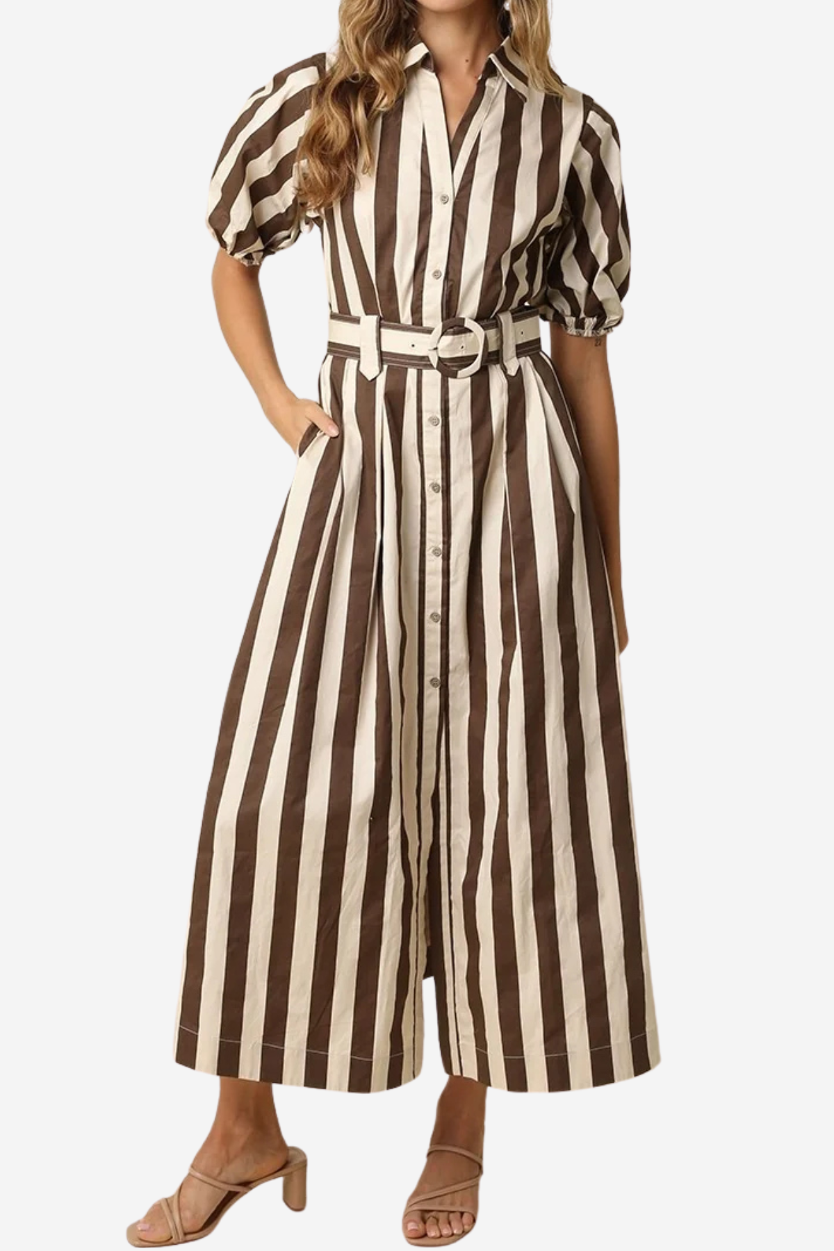 A woman wearing a brown and cream vertical striped midi shirt dress with puff sleeves, a button-up front, and a matching belt, paired with brown heeled sandals against a light gray background.