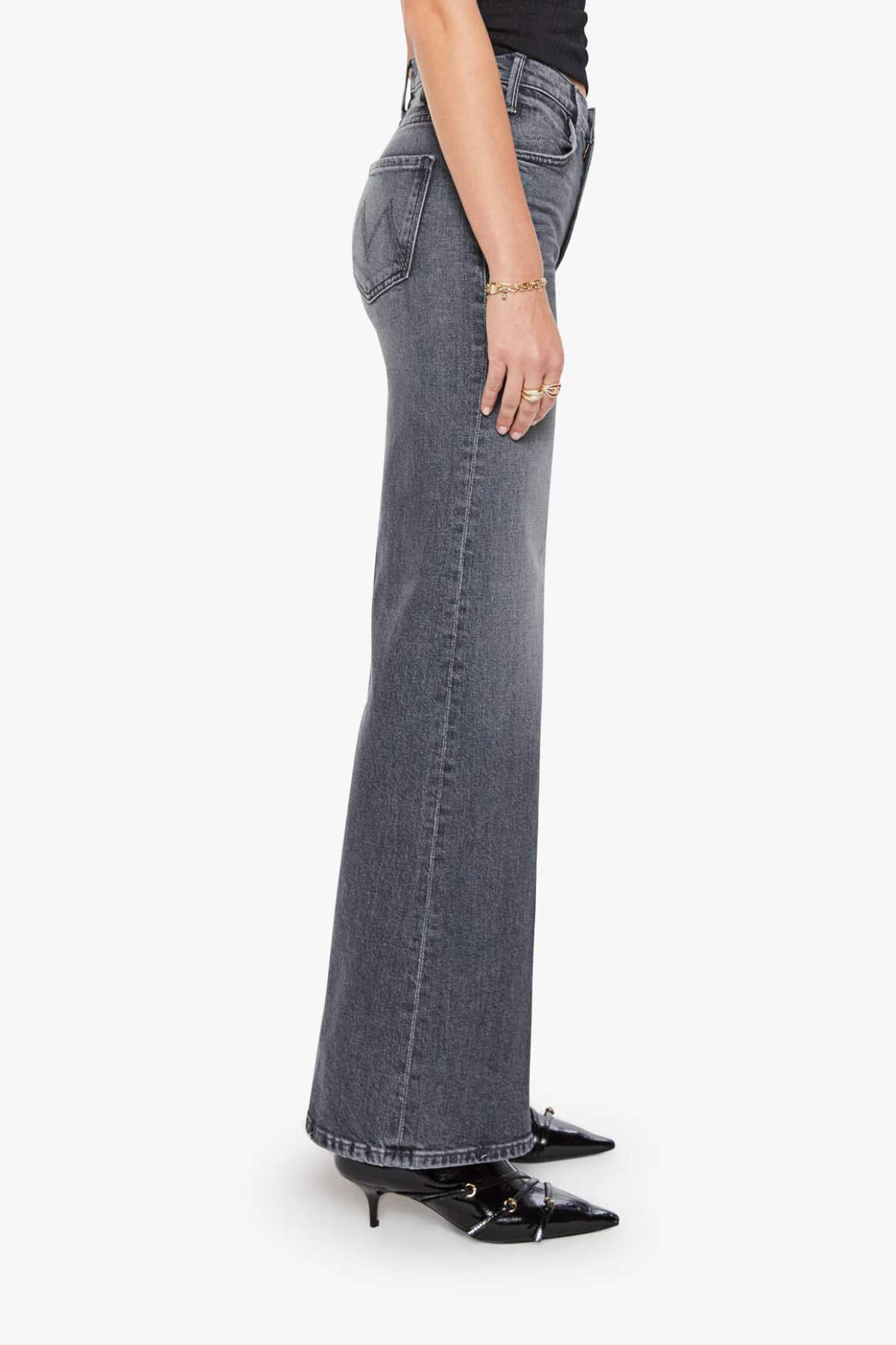 A side profile view of a model wearing high-waisted, wide-leg gray denim jeans with black pointed-toe heels against a plain white background.