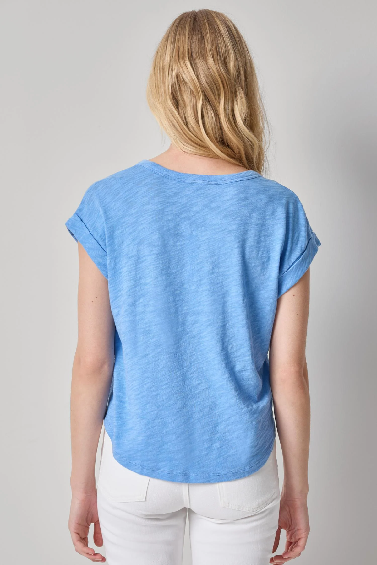 Woman wearing a blue t-shirt and white pants on a gray background
