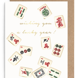 A greeting card with a kraft envelope, featuring illustrated mahjong tiles around gold cursive text that reads 'wishing you a lucky year!'.