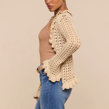 Woman wearing a beige crochet cardigan, brown top, and blue jeans on a beige background
