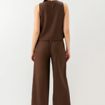 Woman wearing a brown sleeveless top and wide-leg pants on a white background