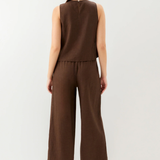 Woman wearing a brown sleeveless top and wide-leg pants on a white background