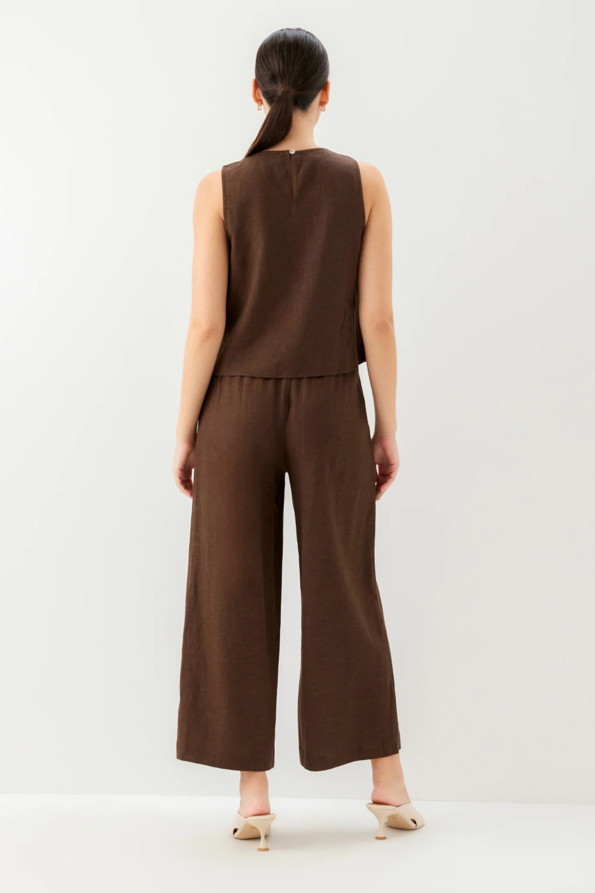 Woman wearing a brown sleeveless top and wide-leg pants on a white background