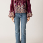 Person wearing a patterned blouse with long sleeves and blue jeans on a white background