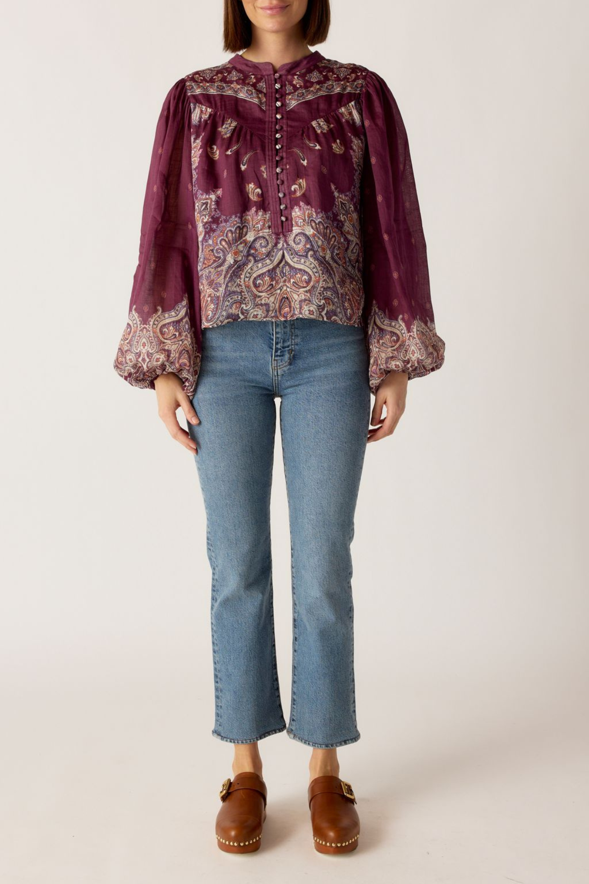 Person wearing a patterned blouse with long sleeves and blue jeans on a white background