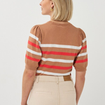 Woman wearing a brown sweater with red and white stripes and beige pants on a white background