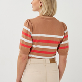Woman wearing a brown sweater with red and white stripes and beige pants on a white background